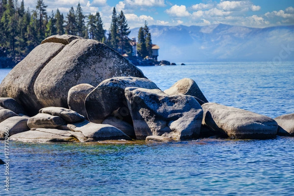 Fototapeta Granite boulders along the shore of Bonsai Rock at Lake Tahoe Nevada USA with clear blue water, pine trees and Sierra Nevada mountains under bright summer sky with white clouds on a calm sunny day