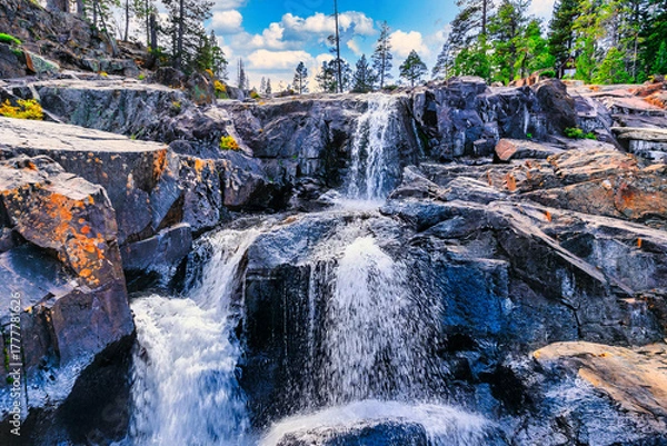 Fototapeta Upper Glen Alpine Falls near Fallen Leaf Lake at Lake Tahoe California USA with cascading mountain water over dark volcanic rocks covered with orange moss and surrounded by pine forest under blue sky