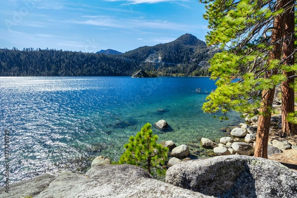 Fototapeta Crystal clear blue water of Emerald Bay at Lake Tahoe California USA with pine trees granite rocks and distant Fannette Island framed by forested Sierra Nevada mountains on bright sunny day
