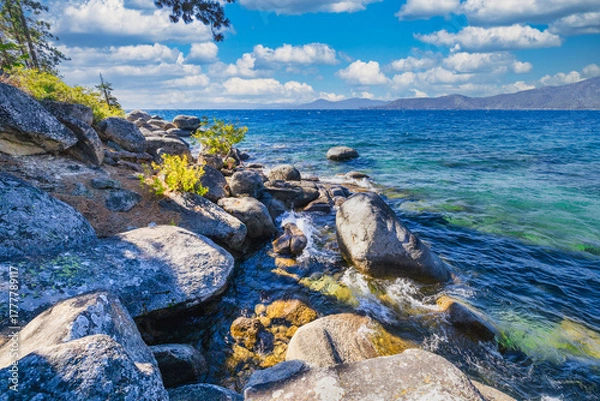 Fototapeta Lake Tahoe California USA scenic rocky shoreline with clear blue water and large granite boulders under bright sky and white clouds summer view of pristine Sierra Nevada nature and landscape