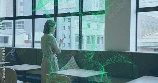 Obraz Standing woman in dress holding phone, looking through window at cafe lounge, copy space