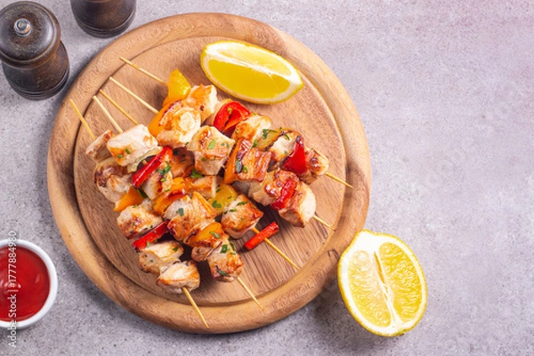 Fototapeta Delicious grilled chicken skewers with capsicum, lemon, salad and ketchup on a plate over the table. Chicken kebab. Healthy food concept.