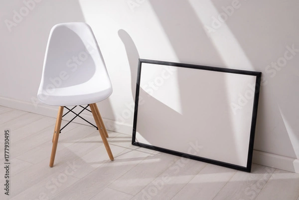 Obraz Mockup of empty frame in modern minimalist interior with chair and morning light on white wall background. Template for artwork, painting, photo or poster