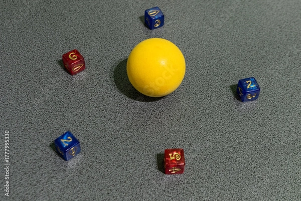 Fototapeta Yellow ball surrounded by colorful dice on a gray surface, symbolizing balance, creativity, randomness, and game strategy in a minimalist composition