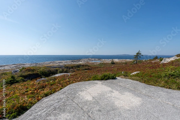 Fototapeta Nova Scotia, Canada - October 06, 2025: Driving toward Peggys Cove, a classic Nova Scotia scene appears: a coastal beach with a small house and a fishing boat, glowing under clear autumn skies.