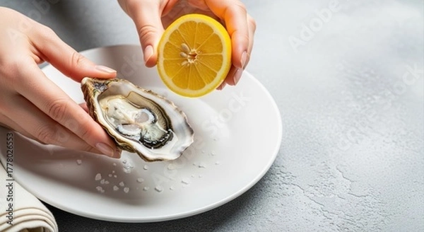 Obraz person squeezing lemon juice on fresh oyster ready to eat on white plate in restaurant