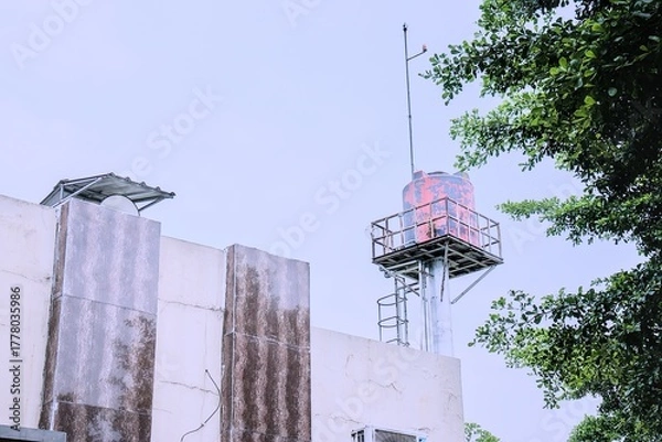 Obraz Water tower rises above building with tree branches in the foreground