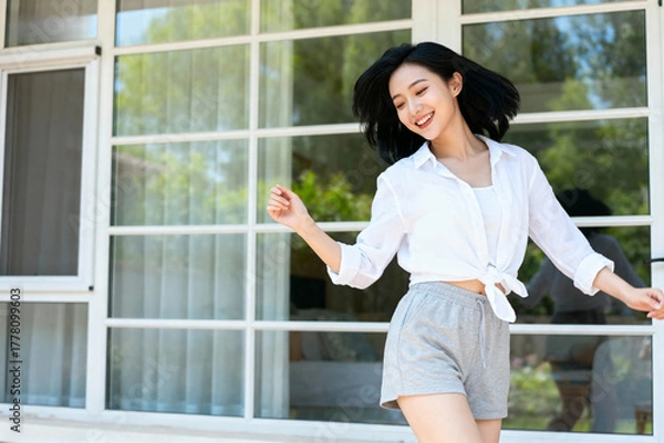 Fototapeta A young woman in casual clothing standing outdoors with a bright smile