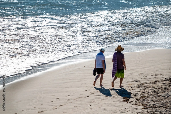 Fototapeta Active senior Australian couple stroll on a beach along the Pacific ocean