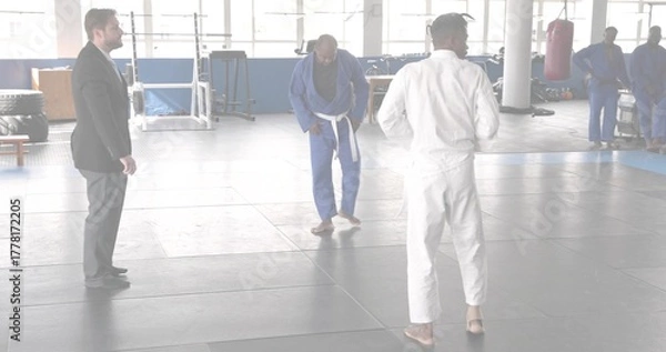 Fototapeta Demonstrating instructor wearing white gi teaching students on dojo mat, with punching bags