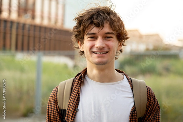 Obraz Portrait of smiling young man wearing backpack in urban setting