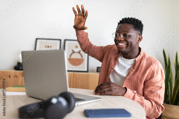 Obraz Young man waving goodbye during video call on laptop at home