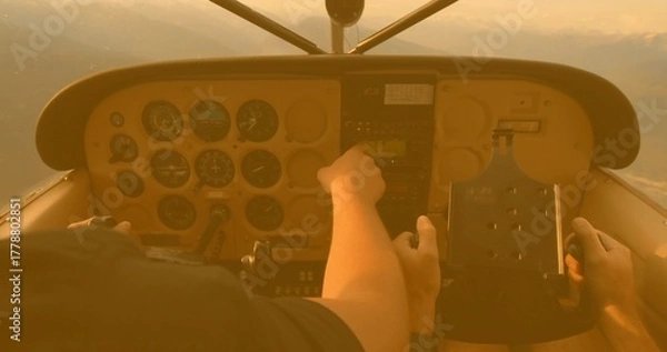 Obraz Pilot and co-pilot adjusting panel controls during sunset flight, with radio stack and yoke