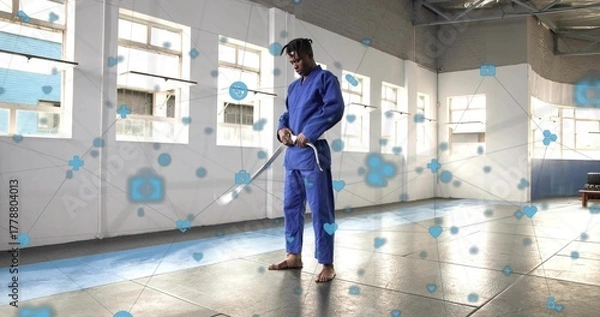 Fototapeta Adjusting stance martial artist wearing blue gi holding wooden sword in dojo, with digital overlay