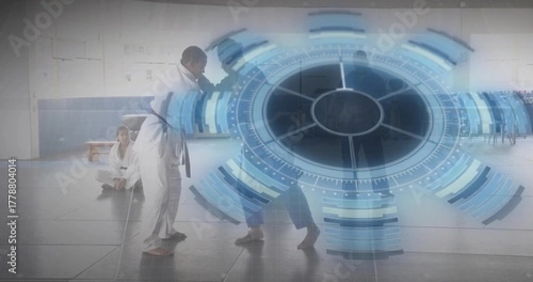 Fototapeta Sparring fighters in uniforms and colored belts engaging strikes in dojo, with digital HUD overlay