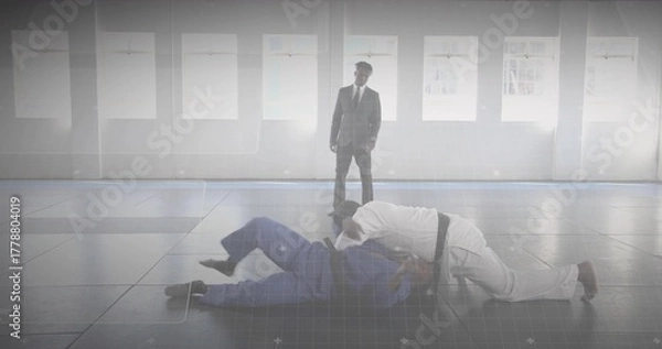 Fototapeta Grappling artists in gis on tatami mats near windows, with coach in suit watching