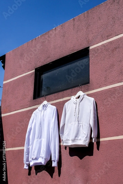 Fototapeta Crisp White Hoodies Hanging on Textured Pink Wall Basked in Bright Sunlight