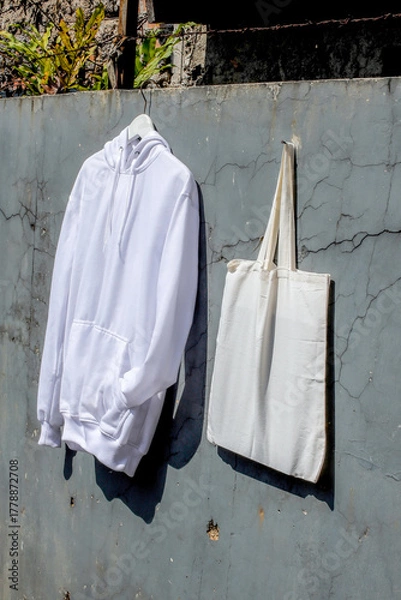 Fototapeta Clean White Hoodie and Tote Bag Hanging Against Rustic Wall