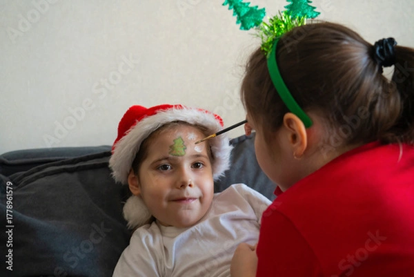Obraz The older sister gives her younger sisters Christmas face painting.