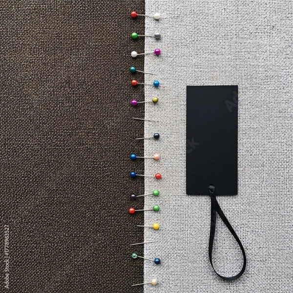 Obraz Neatly aligned vibrant pushpins create a visual boundary between rich brown and light grey textile backgrounds, featuring a sleek black blank label for design