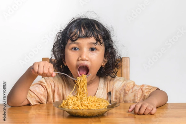 Fototapeta A little Asian girl with curly hair eating fried noodles. Enjoying fried noodles.