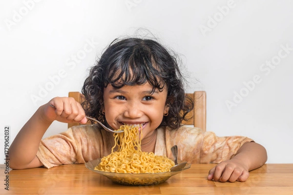 Fototapeta A happy little Asian girl eating fried noodles. A plate of fried noodles.