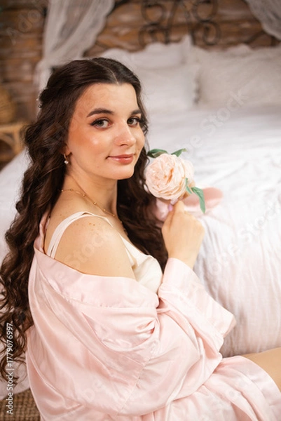 Obraz A beautiful bride poses gracefully by a sunlit window, wearing a delicate lace robe. The light highlights her serene expression and the intricate details of her bridal attire
