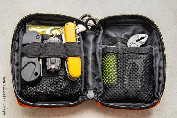 Obraz Open orange EDC pouch with multitool, flashlight, lighter, and other survival gear. Everyday carry organizer