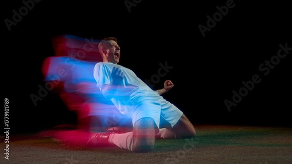 Fototapeta Soccer player celebrating goal on knees with red and blue motion streaks. Concept of passion, victory, and energy applied in sport marketing, motivation, and emotional advertising design.