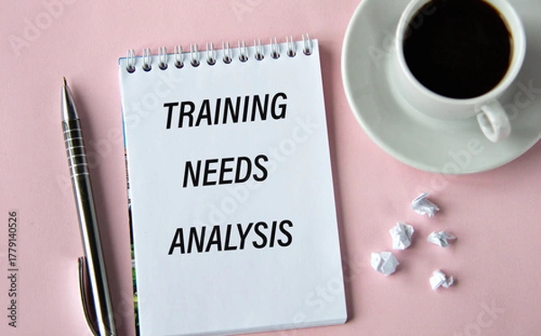 Fototapeta TRAINING NEEDS ANALYSIS - words in a notebook on a pink background with a cup of coffee