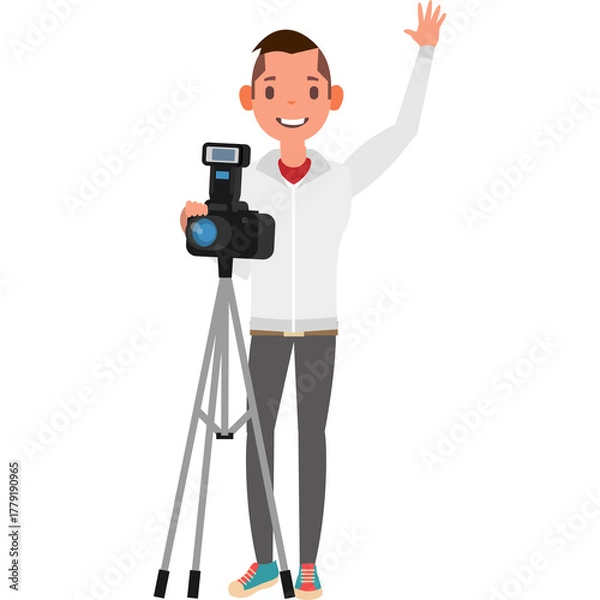 Fototapeta Smiling young man wearing a white jacket and grey pants holding a camera on a tripod waving hello with a white background