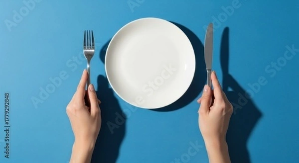 Obraz Hands flanking an empty plate with a fork and knife on a blue surface