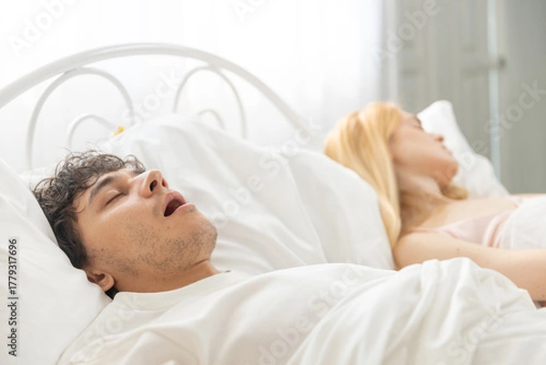 Fototapeta man snoring while sleeping in bed next to woman, close up view showing sleep disorder or breathing problem, concept of snoring, couple sleep issue and nighttime disturbance.