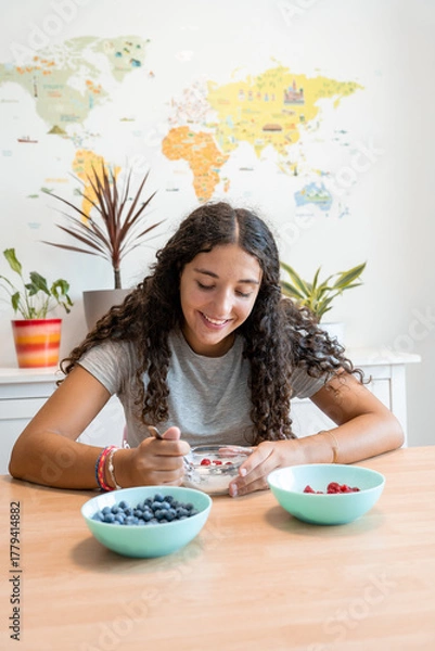 Obraz Smiling young woman eating yogurt with fresh berries at home