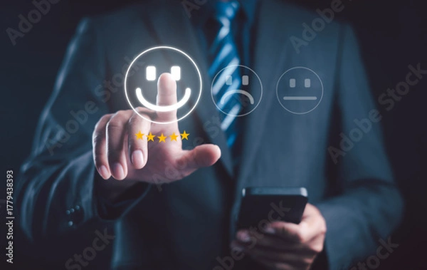 Fototapeta Businessman using smartphone to give five star rating with happy face icon, representing customer satisfaction, feedback, online review, and service quality evaluation concept.