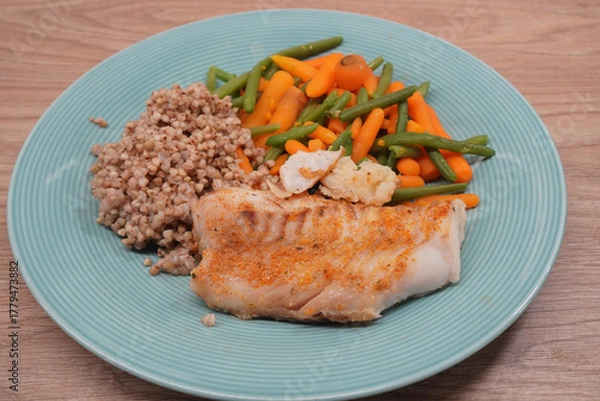 Obraz Delicious baked cod fillet with vegetables and buckwheat on a blue plate