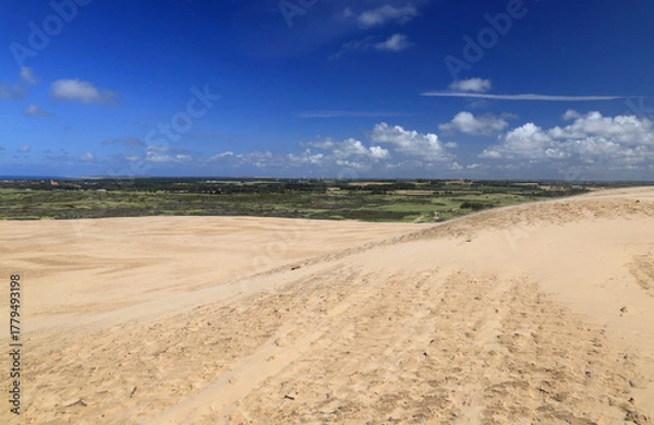 Fototapeta Landscape photo with a view of sand dunes in the foreground against a blue sky with clouds near the Rubjerg Knude lighthouse in Denmark
