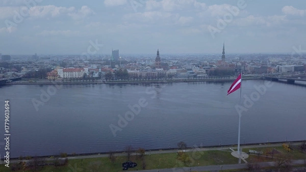 Fototapeta Drone View Of Riga Old Town With Latvian Flag Waving In Foreground Aerial Panorama Of Historic City Center, Daugava River And Urban Skyline On A Outumn Day In Latvia