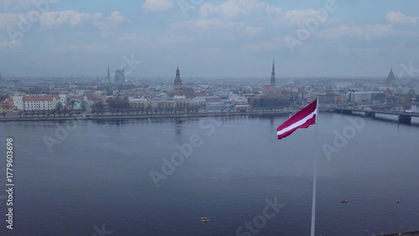 Fototapeta Drone View Of Riga Old Town With Latvian Flag Waving In Foreground Aerial Panorama Of Historic City Center, Daugava River And Urban Skyline On A Outumn Day In Latvia