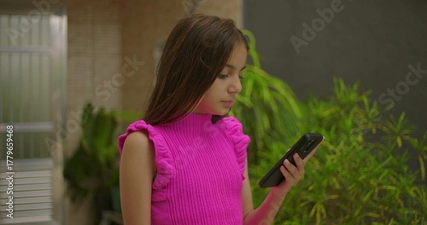 Fototapeta Young girl focused on smartphone screen in outdoor environment, engaging with technology, browsing, or interacting with digital content in a thoughtful manner