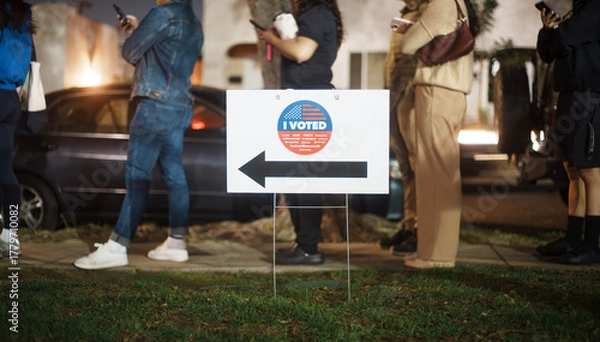 Fototapeta Elections in the USA.  "I Voted" sign with voters standing in line in the background as many people are voting late at night.