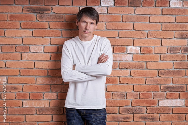 Fototapeta Portrait of a middle-aged European man in a white shirt near a brick wall