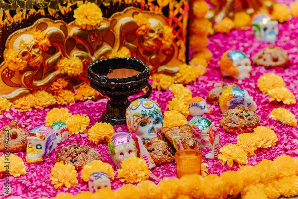 Fototapeta Close view of Day of the Dead offerings featuring decorated sugar skulls, Pan de Muerto (bread of the dead), and marigold flowers on a vibrant background.