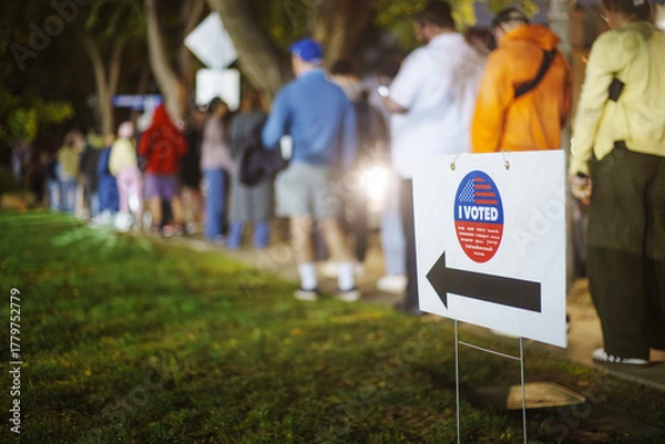 Fototapeta Elections in Los Angeles, California. "I Voted" sign with voters standing in line on sidewalk in the background as many people are voting late at night.