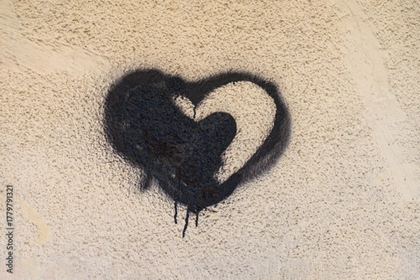 Fototapeta Black heart graffiti with dripping spray paint on textured beige wall, creating a raw street art aesthetic. Emotional background, rebellious urban expression, underground street art