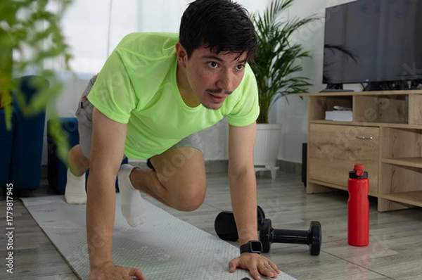 Obraz Man performing a mountain climber exercise from a frontal angle on a mat in his living room. Home workout, cardio, energy, and healthy lifestyle
