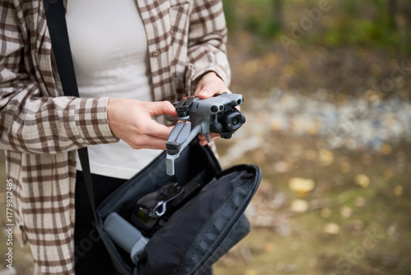 Fototapeta A person stands in a natural setting, carefully taking a drone from a bag, excited for the aerial exploration ahead.