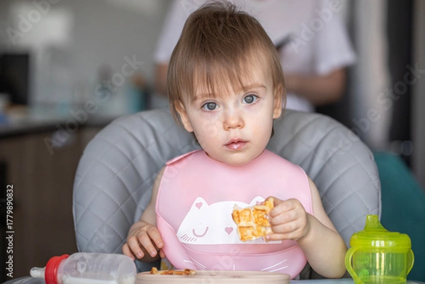 Obraz Infant girl eats deliciously while sitting at a childrens table