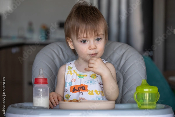 Obraz Infant girl eats deliciously while sitting at a childrens table