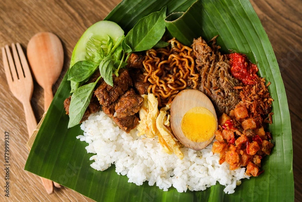 Fototapeta Nasi langgi is an Indonesian dish, served with rice and various side dishes like shredded beef, eggs, noodles, tempeh, potatoes, spiced grated coconut, chili, cucumber, and lemon basil.